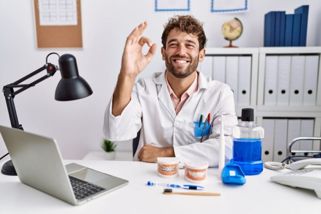 Purpose of an appointment system: Young Hispanic dentist man working in a medical clinic, smiling positively, illustrating the successful implementation of an appointment system in healthcare settings.